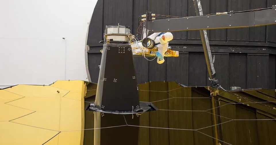 A Ball Aerospace engineer in a cleanroom suit connecting fibre optic cables on the James Webb Space Telescope, the unglamorous connection work behind a flagship system.
